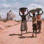 three women carrying basin while walking barefoot