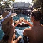 Man and Woman Sitting on Swimming Pool while Holding a Glass of Wine