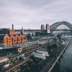 aerial photography of concrete buildings and bridge beside ocean under cloudy sky