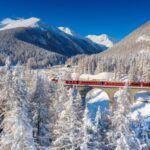 Winter sun over Bernina Express train on viaduct in the snowy landscape, Chapella, Graubunden canton, Engadine, Switzerland