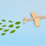 Wooden airplane model emitting fresh green leaves on blue background. Sustainable travel; clean and green energy; and biofuel for aviation industry concept.