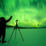 A photographer stands with his tripod while photographing the northern lights over Lake Laberge in Yukon.