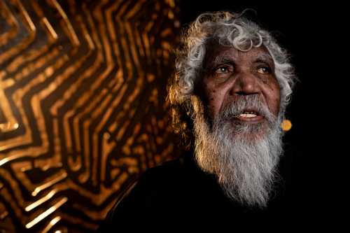 Bobby West Tjupurrula stand in front of his installation Hypnotic Reverberations. Credit Parrtjima 2025