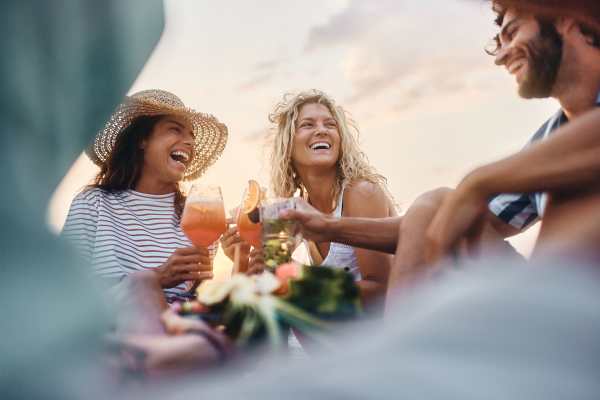Below view of happy friends toasting with cocktails in summer day.