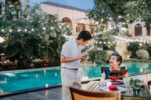 Senior Asian Female Smiling and Ordering Food from Male Asian Waiter at Luxury Poolside Restaurant